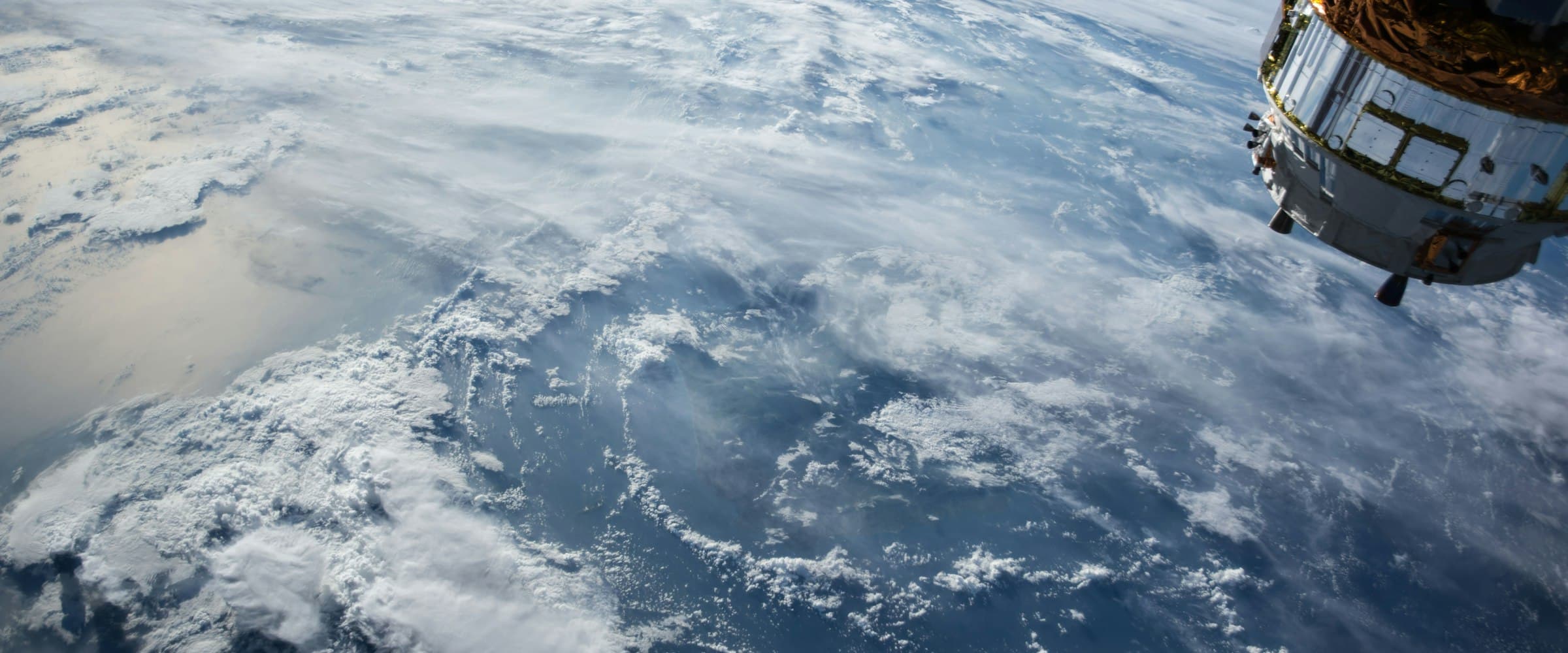 Spacecraft in orbit above Earth, with clouds and ocean below